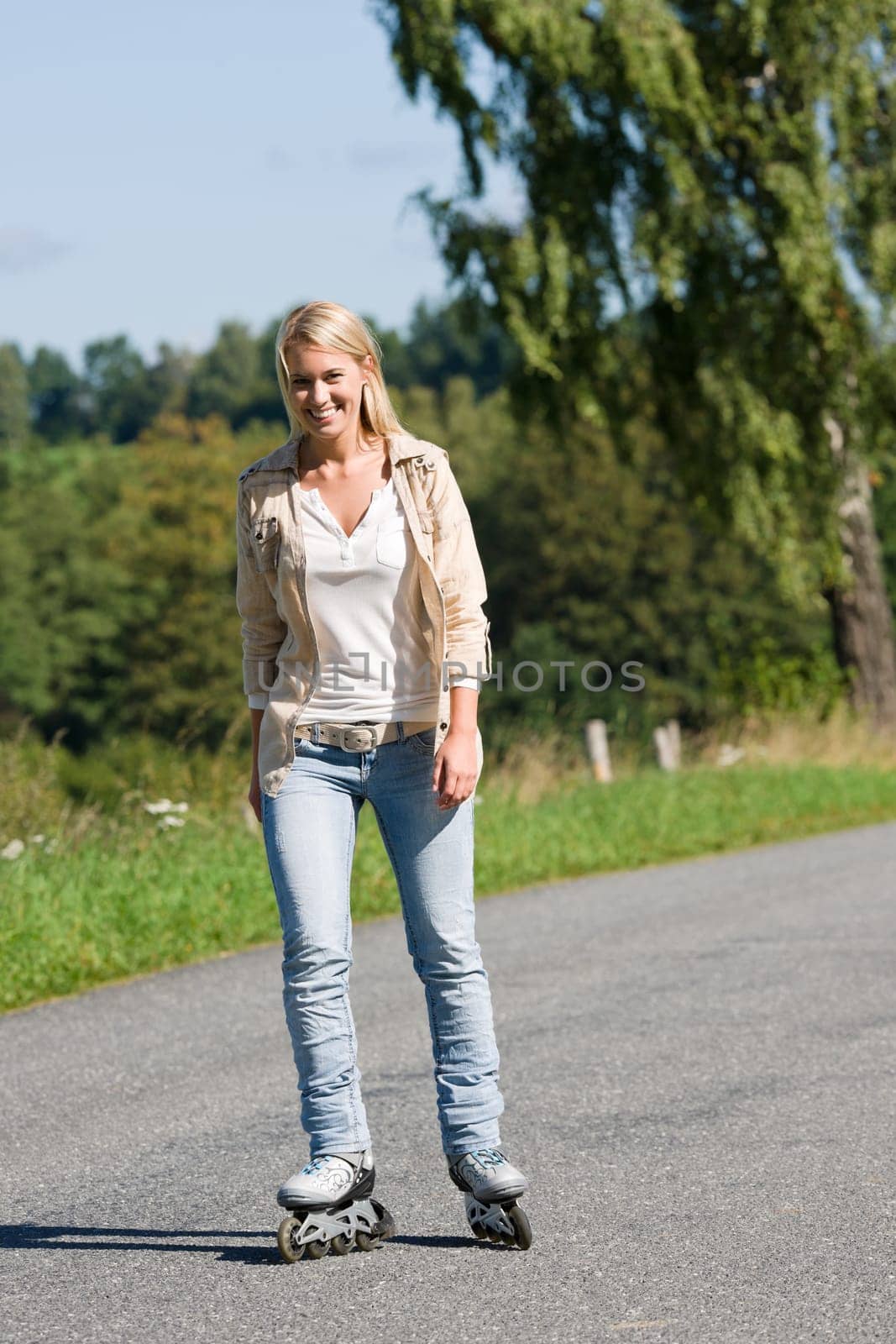 Inline skating young woman wearing jeans on sunny asphalt road