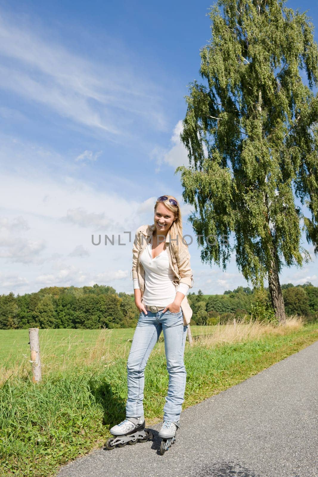Inline skating young woman wearing jeans on sunny asphalt road