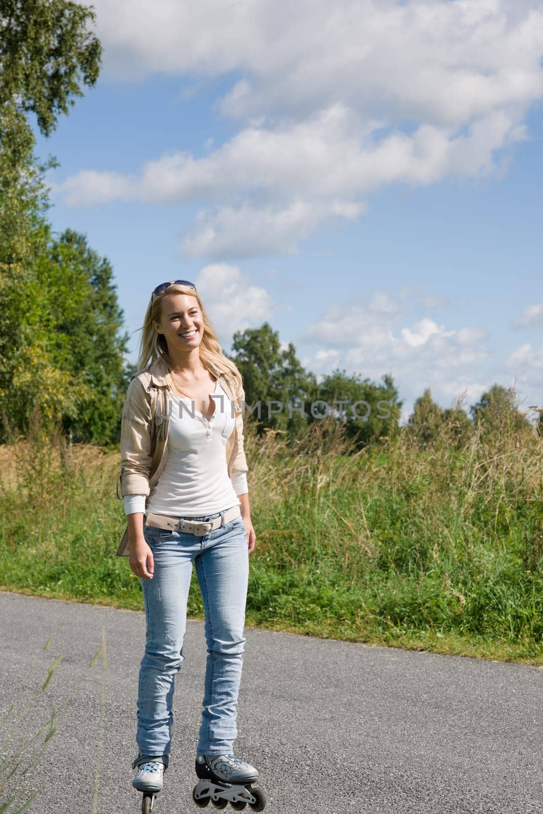 Inline skating young woman wearing jeans on sunny asphalt road