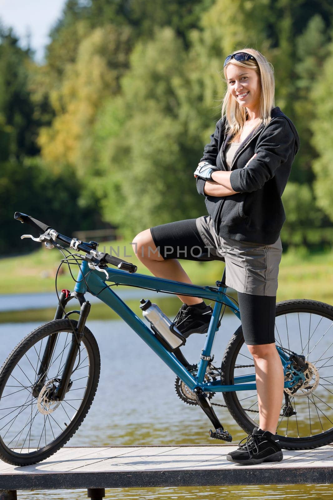 Mountain biking young woman standing on pier looking natural lake