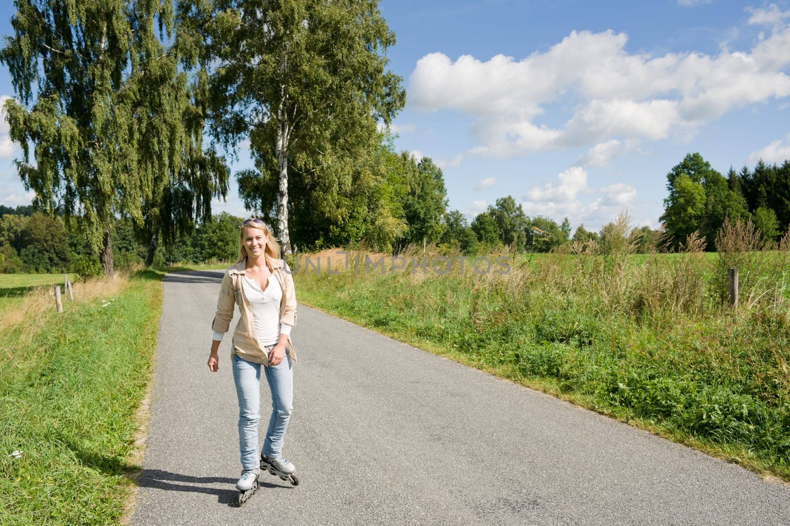 Inline skating young woman wearing jeans on sunny asphalt road
