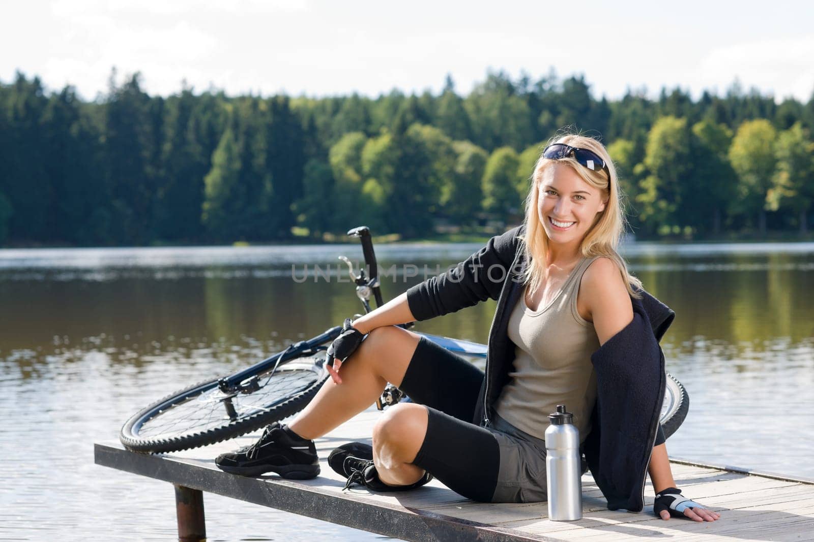 Sport biking young woman sitting on pier by natural lake