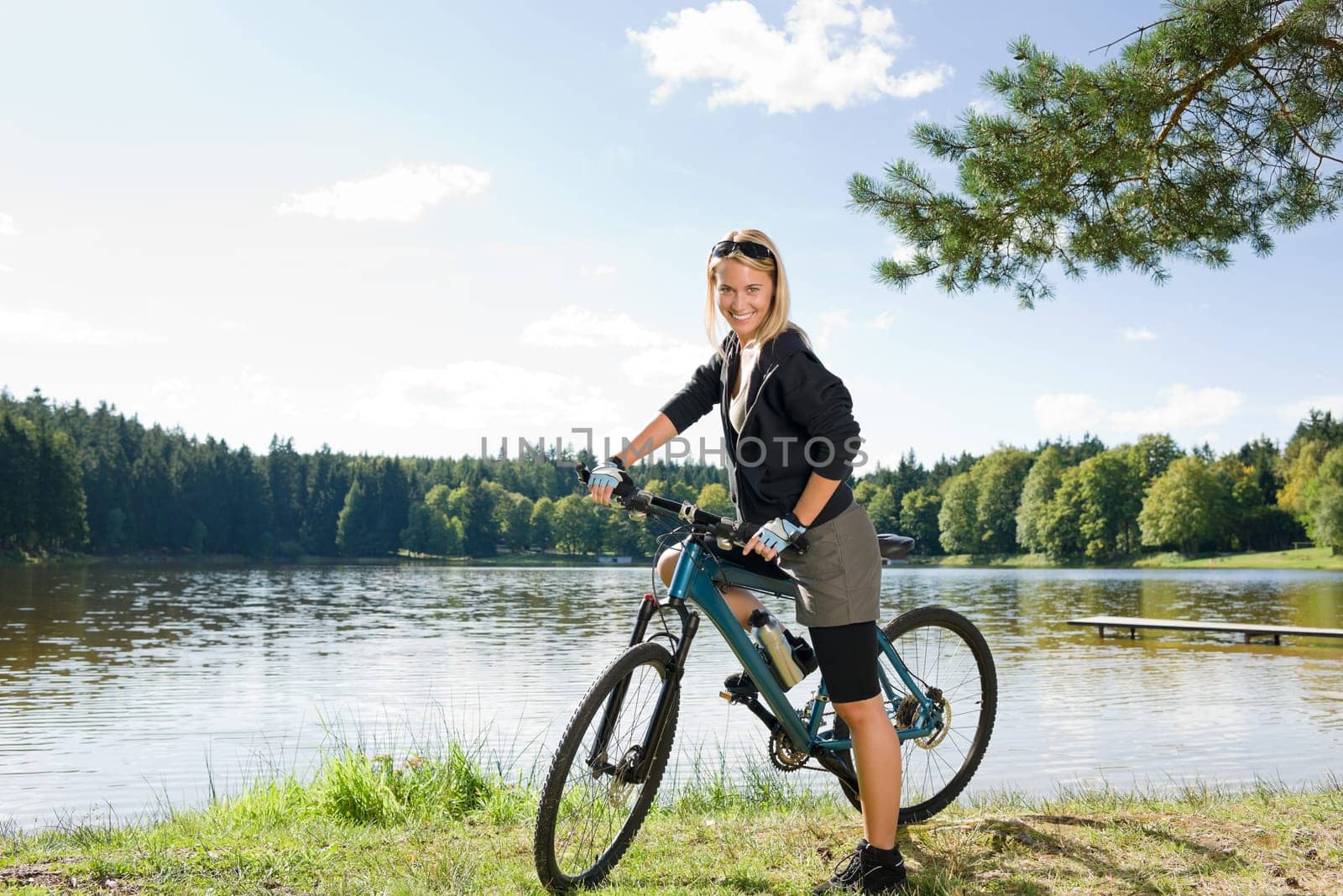 Beautiful young blond woman riding bicycle by lake summer day