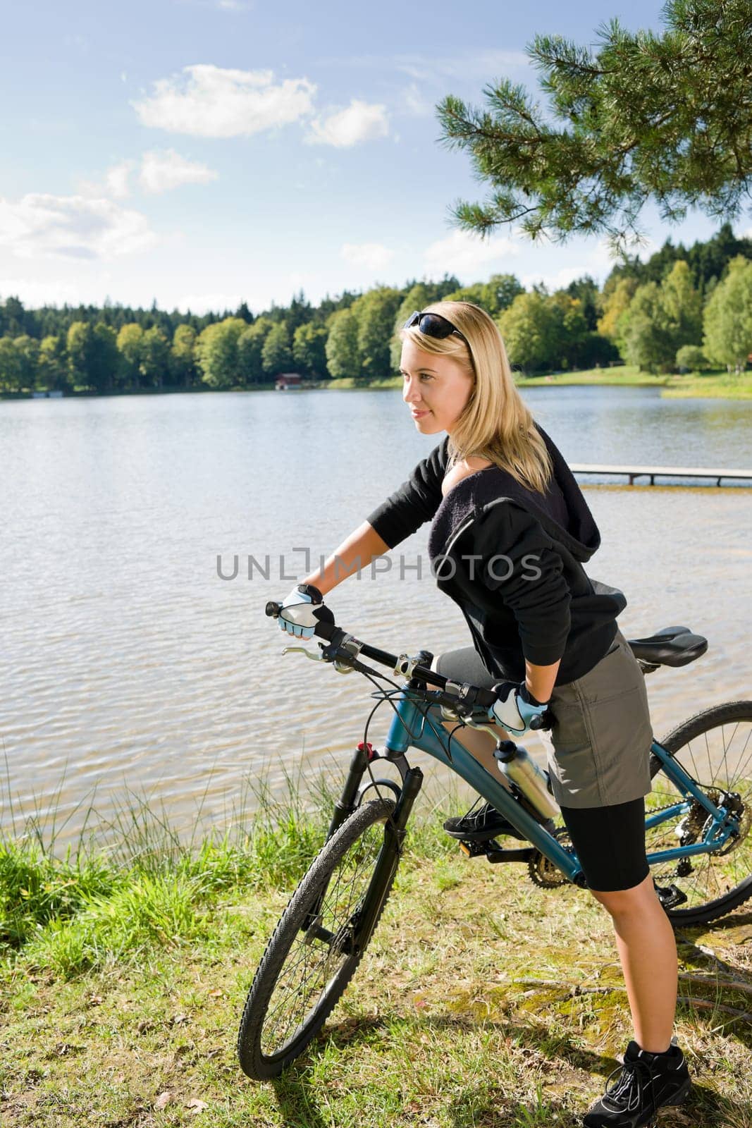 Beautiful young blond woman riding bicycle by lake summer day