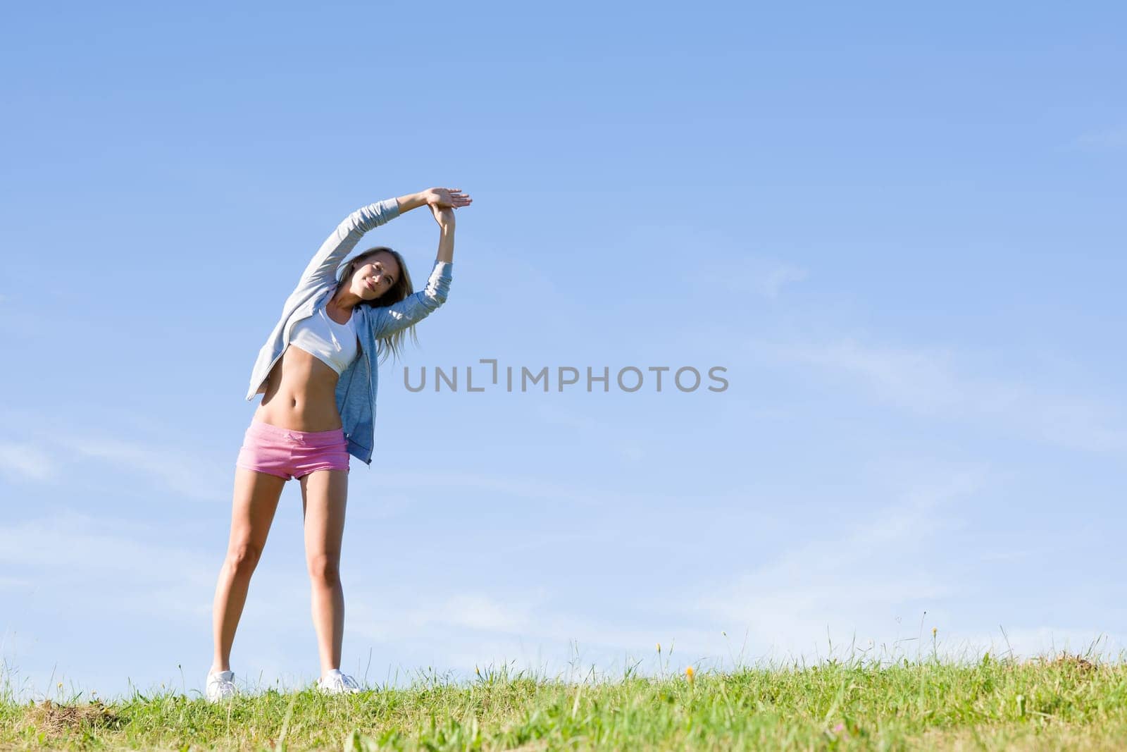 Sportive stretching young happy woman meadows blue summer sky