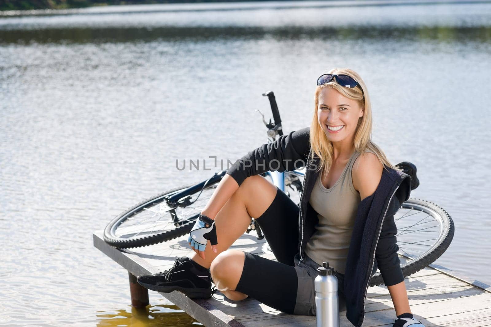Sport biking young woman sitting on pier by natural lake