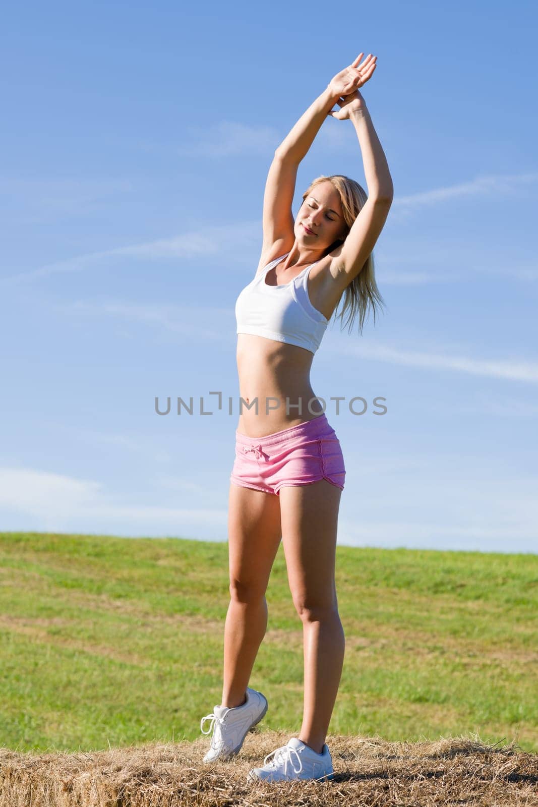 Summer active woman stretching on bales in fitness outfit