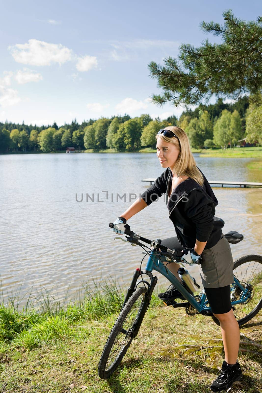 Beautiful young blond woman riding bicycle by lake summer day
