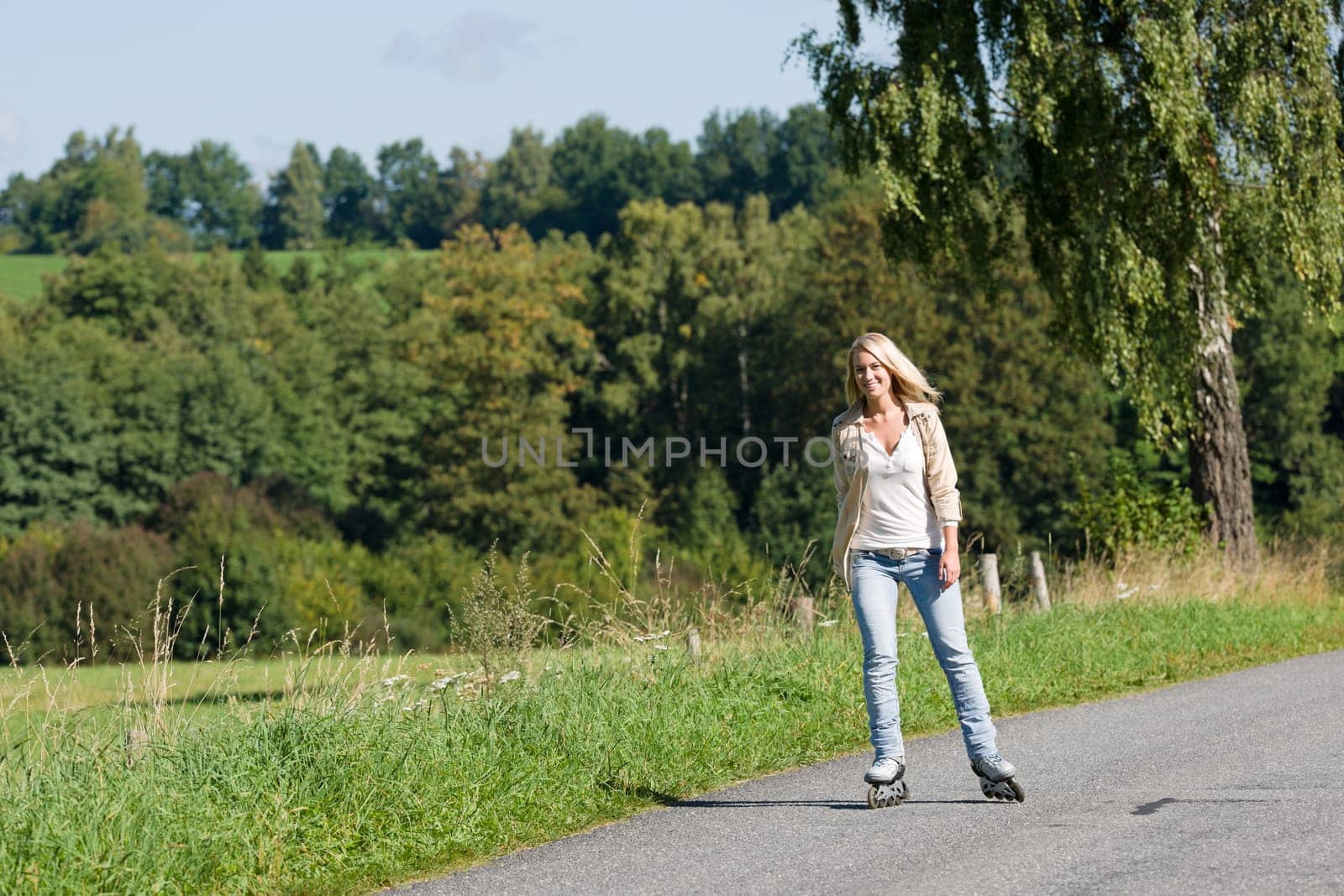 Inline skating young woman wearing jeans on sunny asphalt road