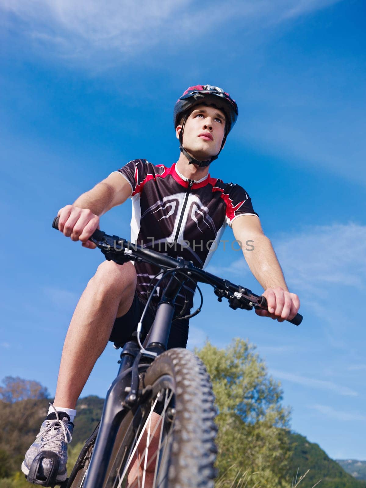 sports activity: young adult cyclist riding mountain bike in the countryside. Vertical shape, low angle view, copy space