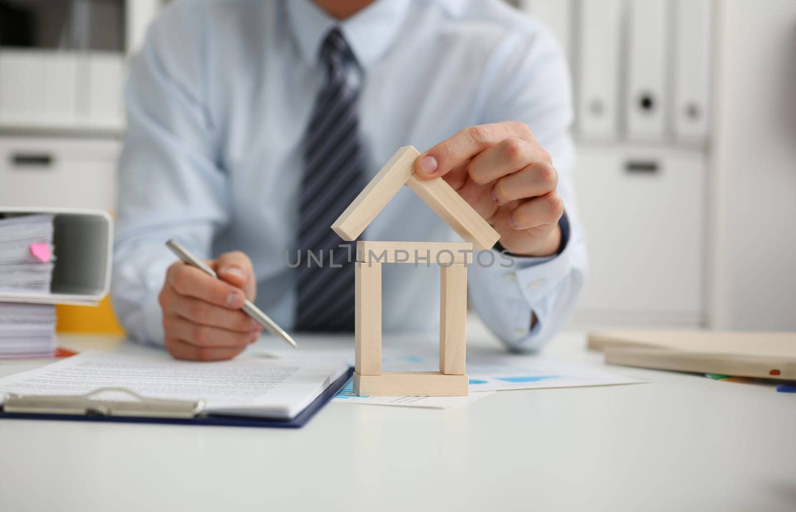 Male hand holds the roof to the lock in the hand against the backdrop of the toy house sale. Purchase lease concept real estate services on the market.