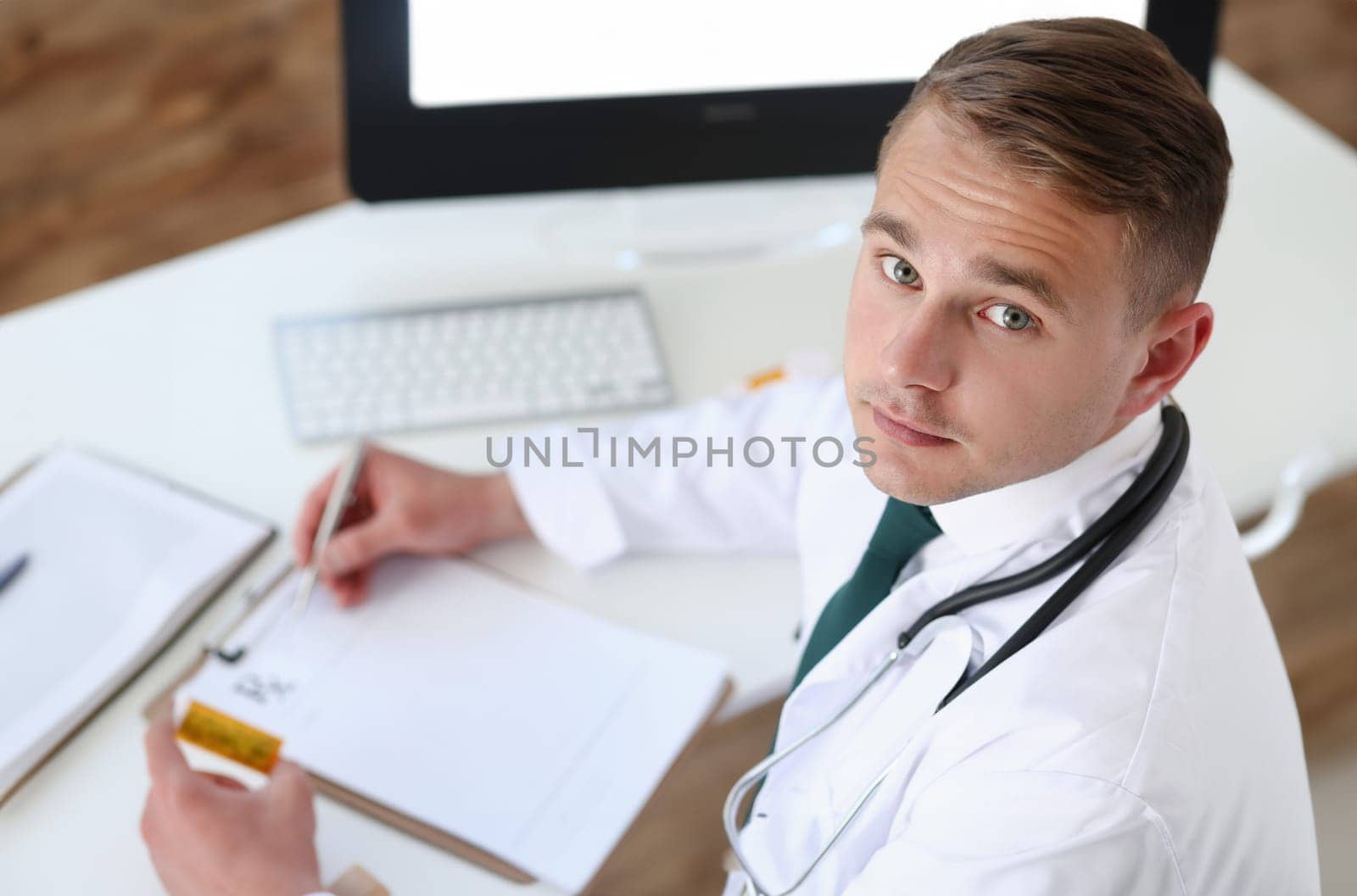 Male medicine doctor hand hold jar of pills and write prescription to patient at worktable. Panacea and life save prescribing treatment legal drug store concept. Empty form ready to be used