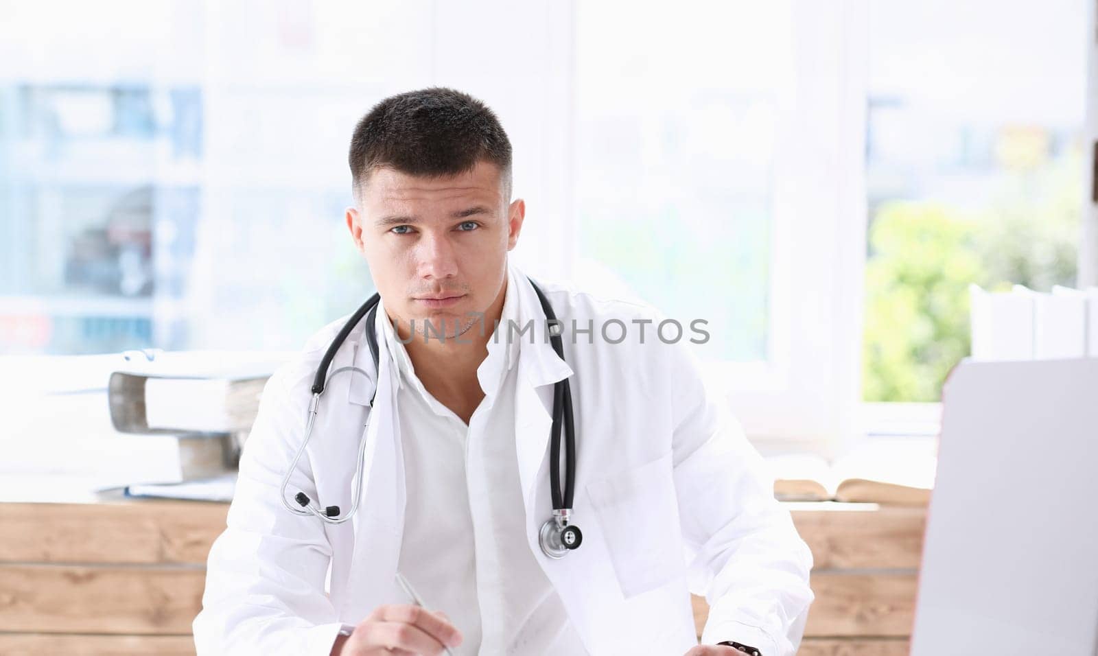 Handsome smiling male doctor sit at workplace in office. Physical and disease prevention patient aid exam visit 911 ward round prescribe remedy healthy lifestyle consultant profession concept