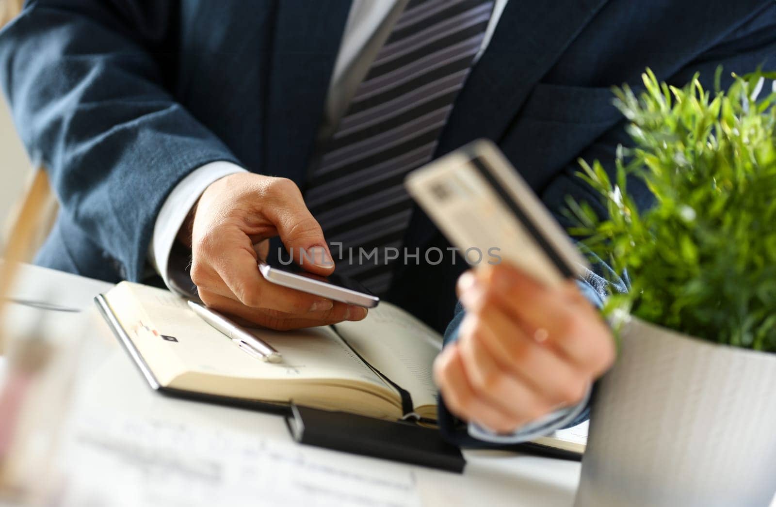 Male arms in suit hold credit card and phone make transfer closeup. Anti-fraud financial security when entering client discount program number or filling personal credential password login to account