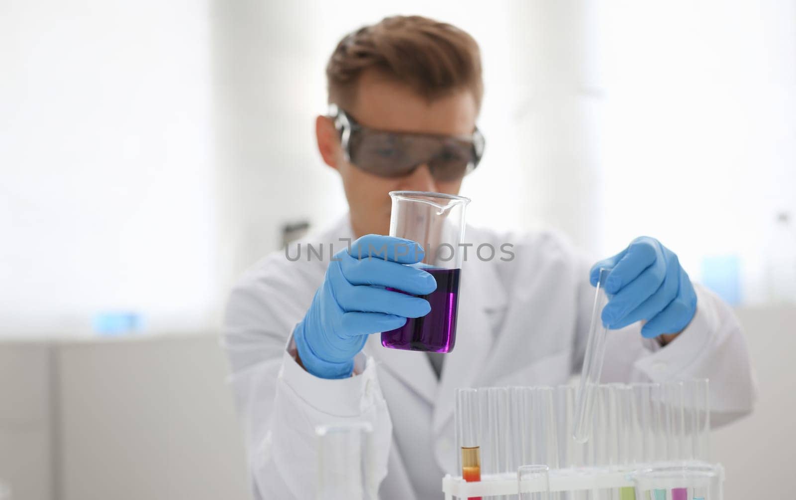 A male chemist holds test tube of glass in his hand overflows a liquid solution of potassium permanganate. Conducts an analysis reaction takes various versions of reagents using chemical manufacturing.