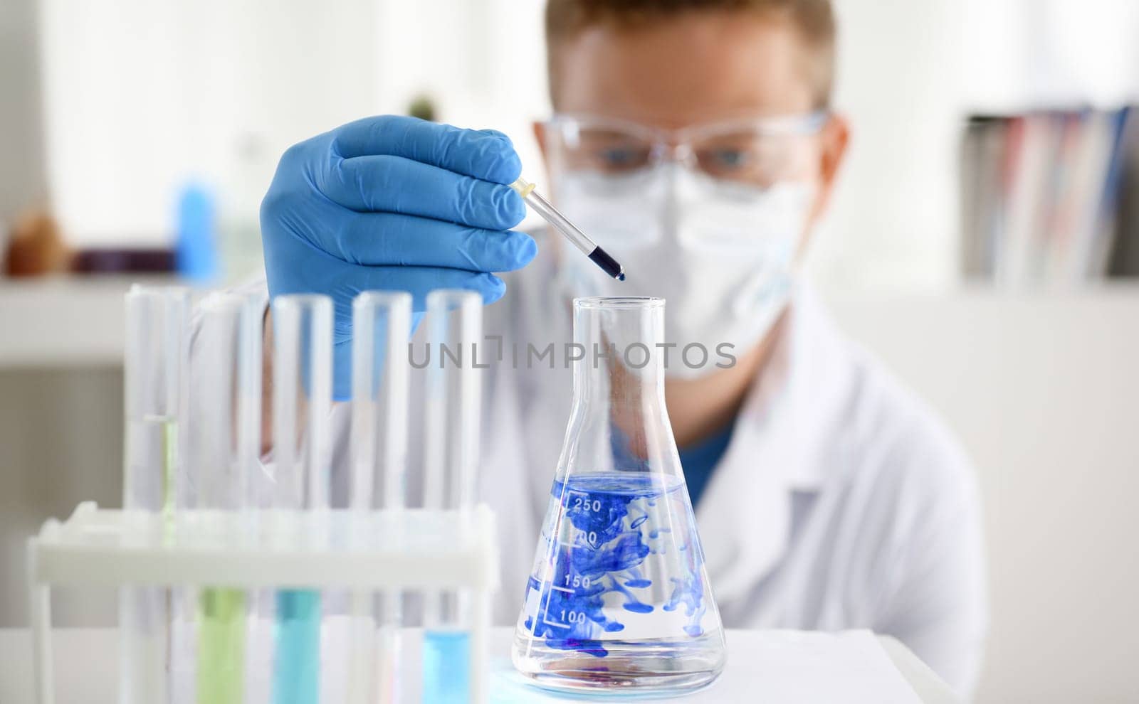 A male chemist holds test tube of glass in his hand overflows a liquid solution of potassium permanganate. Conducts an analysis of water samples versions of reagents using chemical manufacturing.
