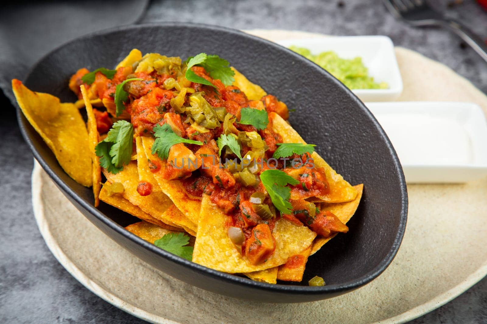 nachos with sauce, meat and herbs in a black plate