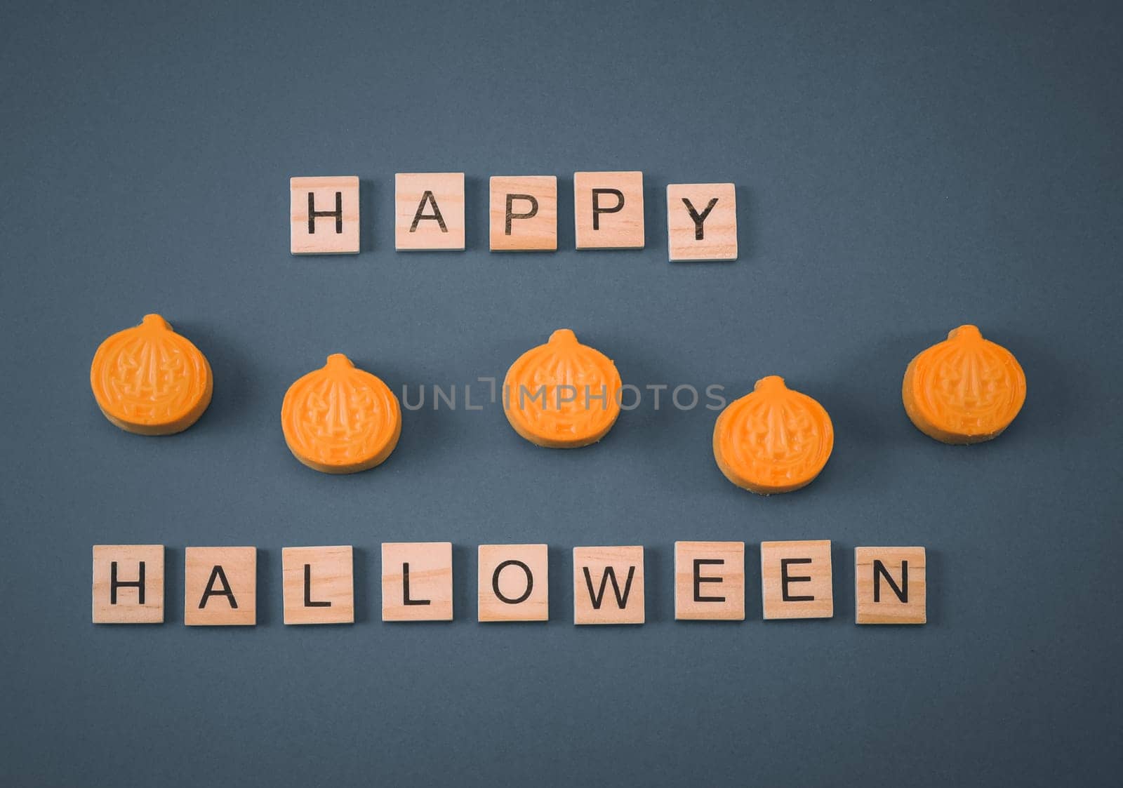 Five small orange chocolate pumpkins and wooden cubes with the inscription: happy halloween lie in a row on a gray background, flat lay close-up. Concept greeting card.
