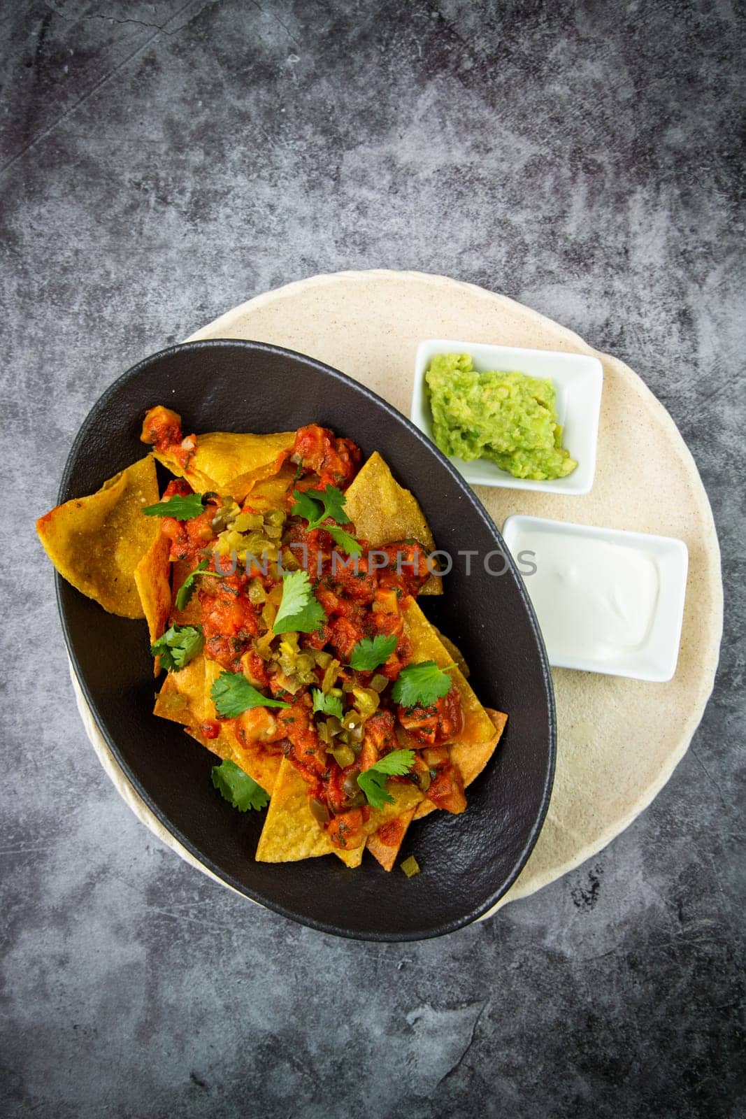 nachos with sauce, meat and herbs in a black plate, top view by tewolf