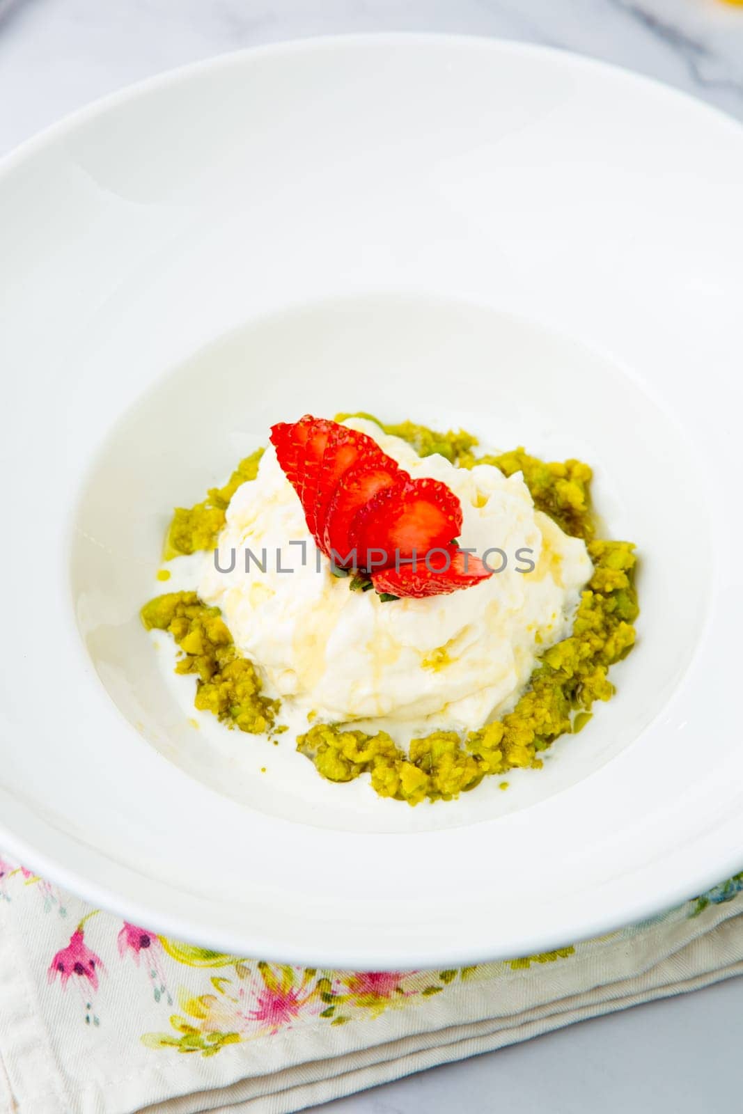 curd dessert with strawberries on top in a white plate on a marble background