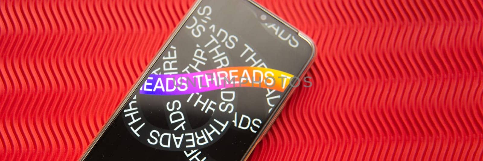 Tver, Russia - July 15, 2023, threads logo on the smartphone screen, on a red background. The threads icon. The logo of the current application. Threads social network. by Annu1tochka