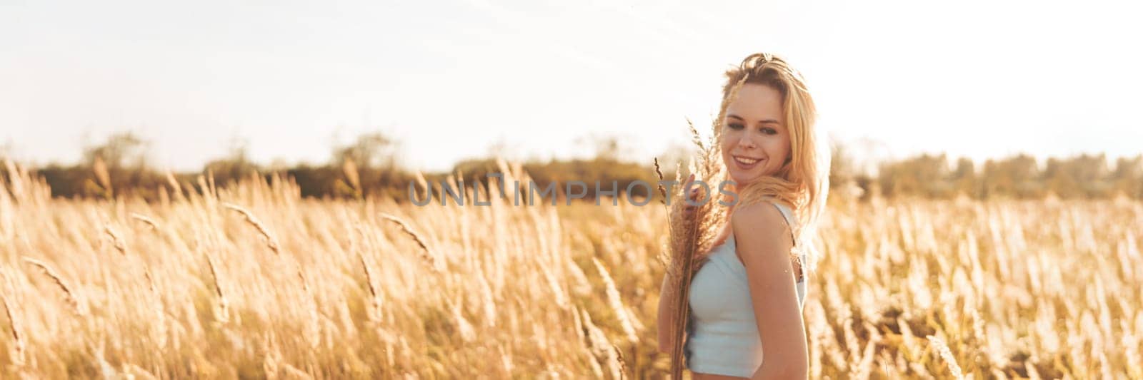 Beautiful blonde woman on a walk in a field with dry grass. A walk in nature, sunset in a field of pampas grass. Life style.