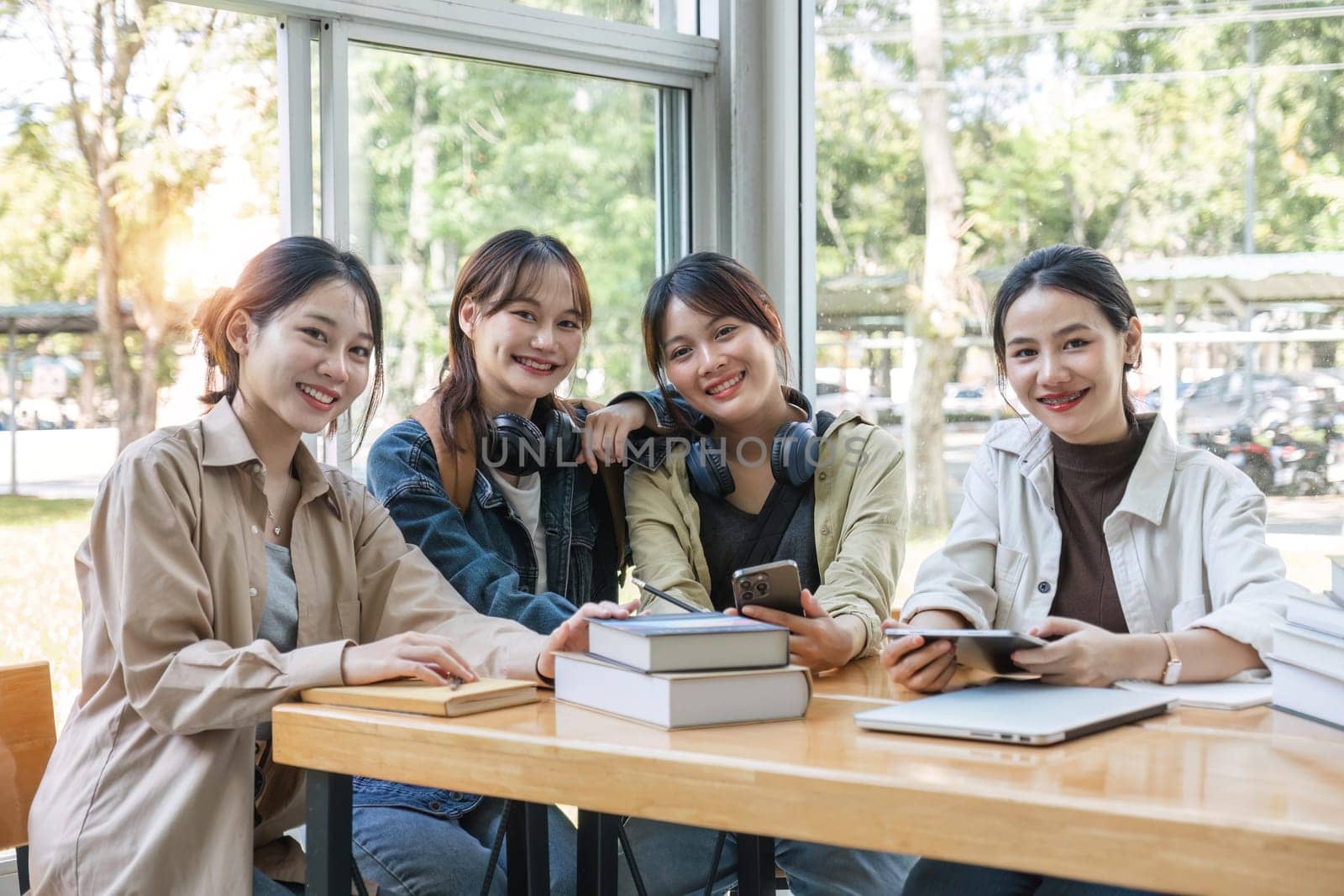 Group of cheerful Asian college students or friends laughing together while sitting in university. by wichayada