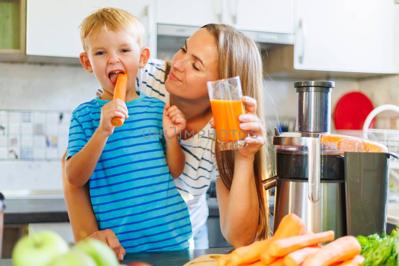 Mom and son drink fresh carrot juice squeezed using a juicer in the kitchen at home. Family nutrition, healthy eating concept