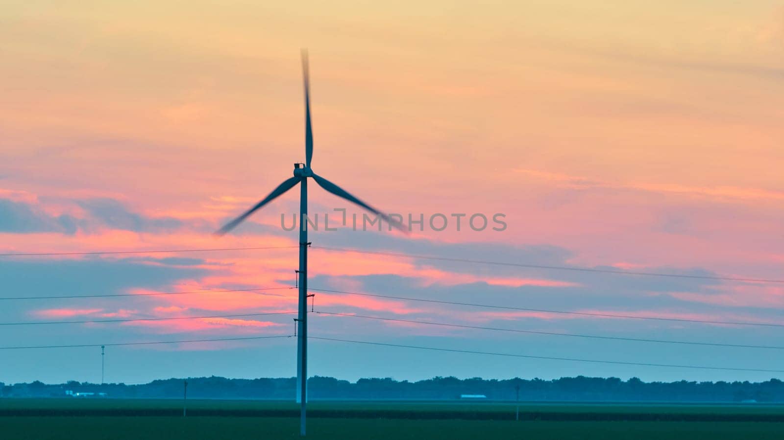 Aerial spinning wind turbine at dusk with pink and blue clouds by njproductions