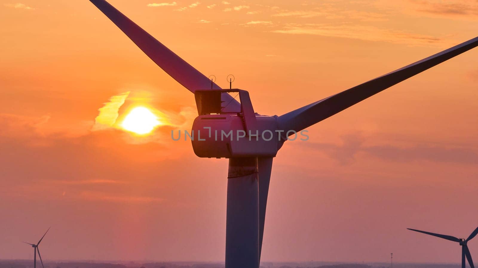 Image of Golden sun at sunset behind close up of top of wind turbine with two distant turbines aerial