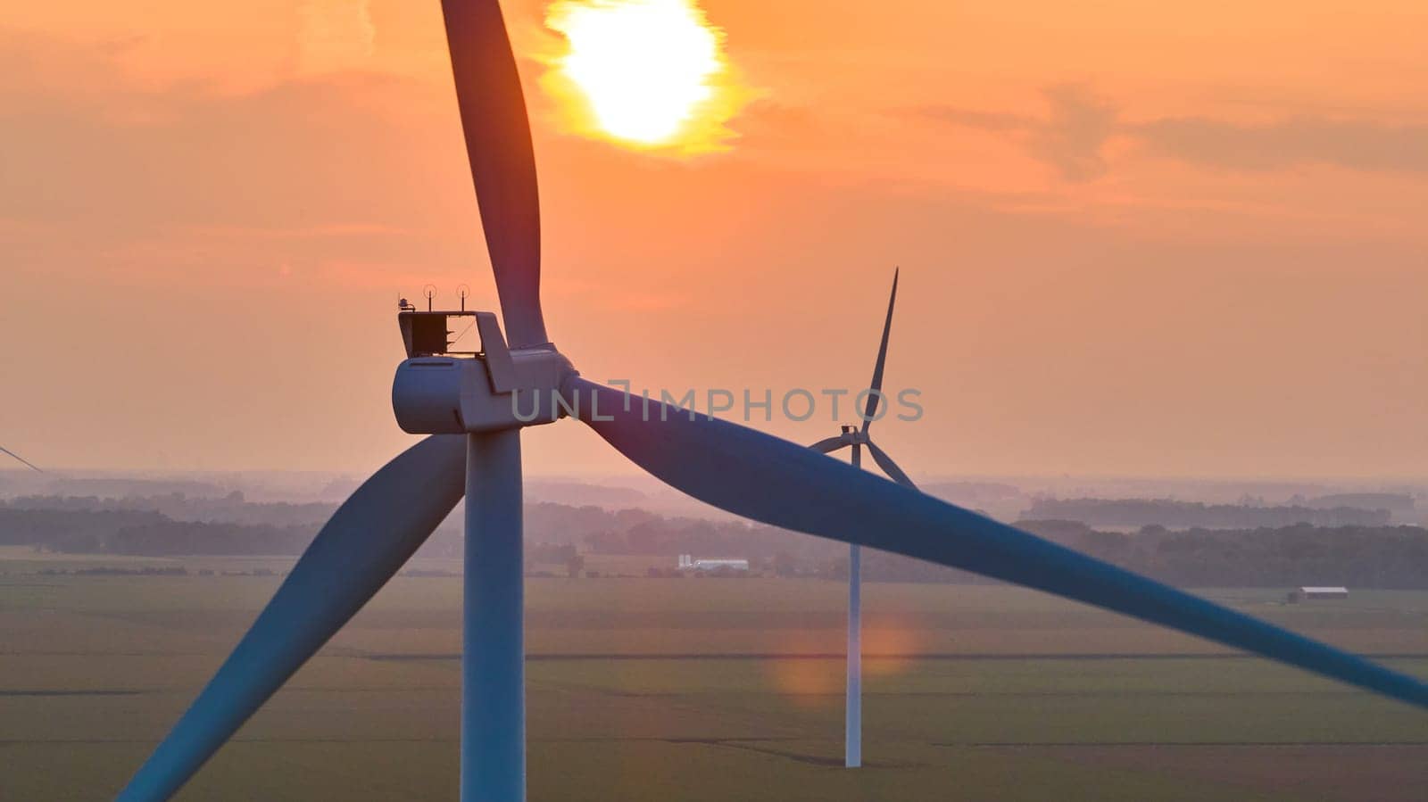 Image of Golden sun at sunrise behind close up of top of wind turbine with distant turbine aerial