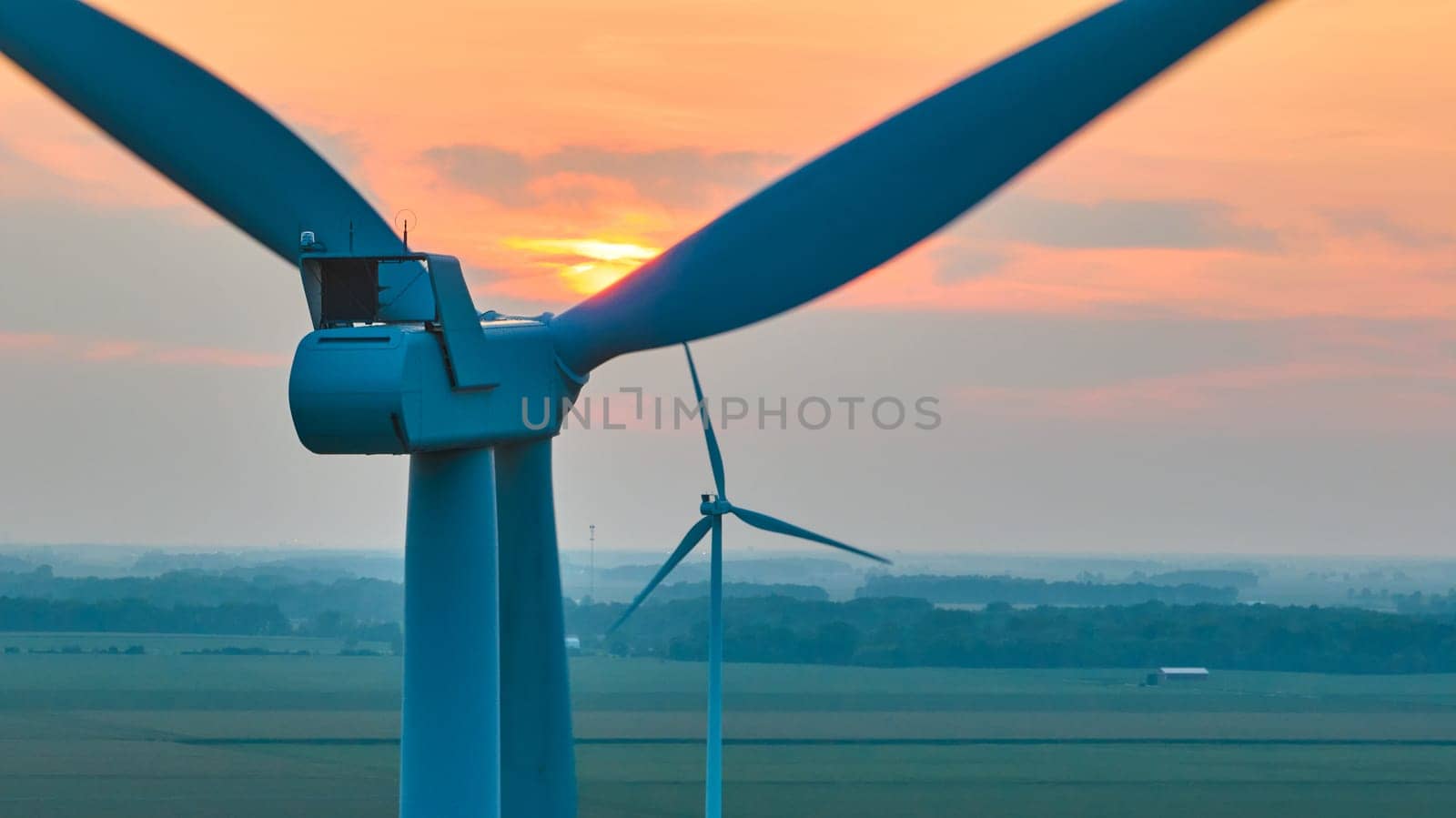 Image of Golden sun setting over top of wind turbine in straight on aerial