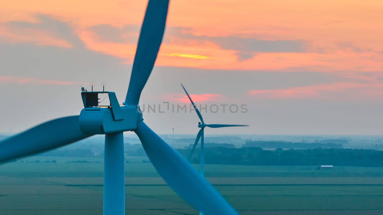 Two wind turbines at sunset on hazy day aerial over farmland by njproductions