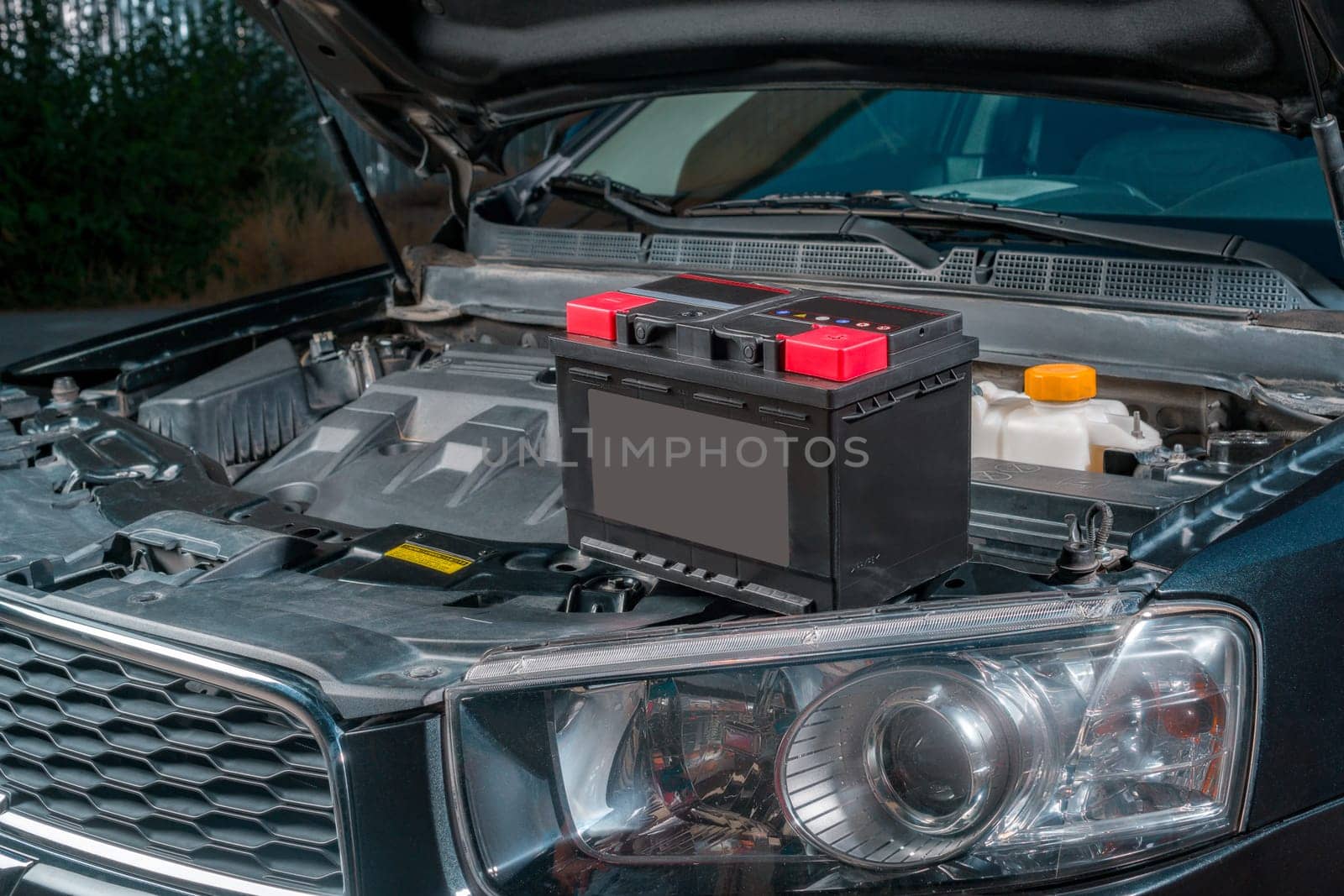 A new battery sits on the engine of a car with the hood open by A_Karim