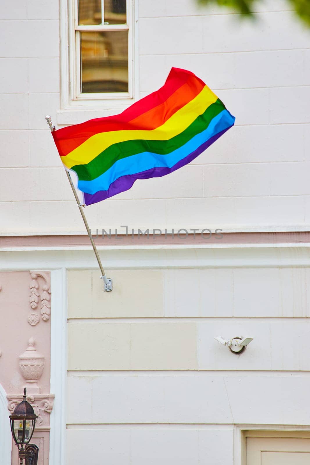 Image of Rainbow pride flag stretched out in the wind against white building with white garage