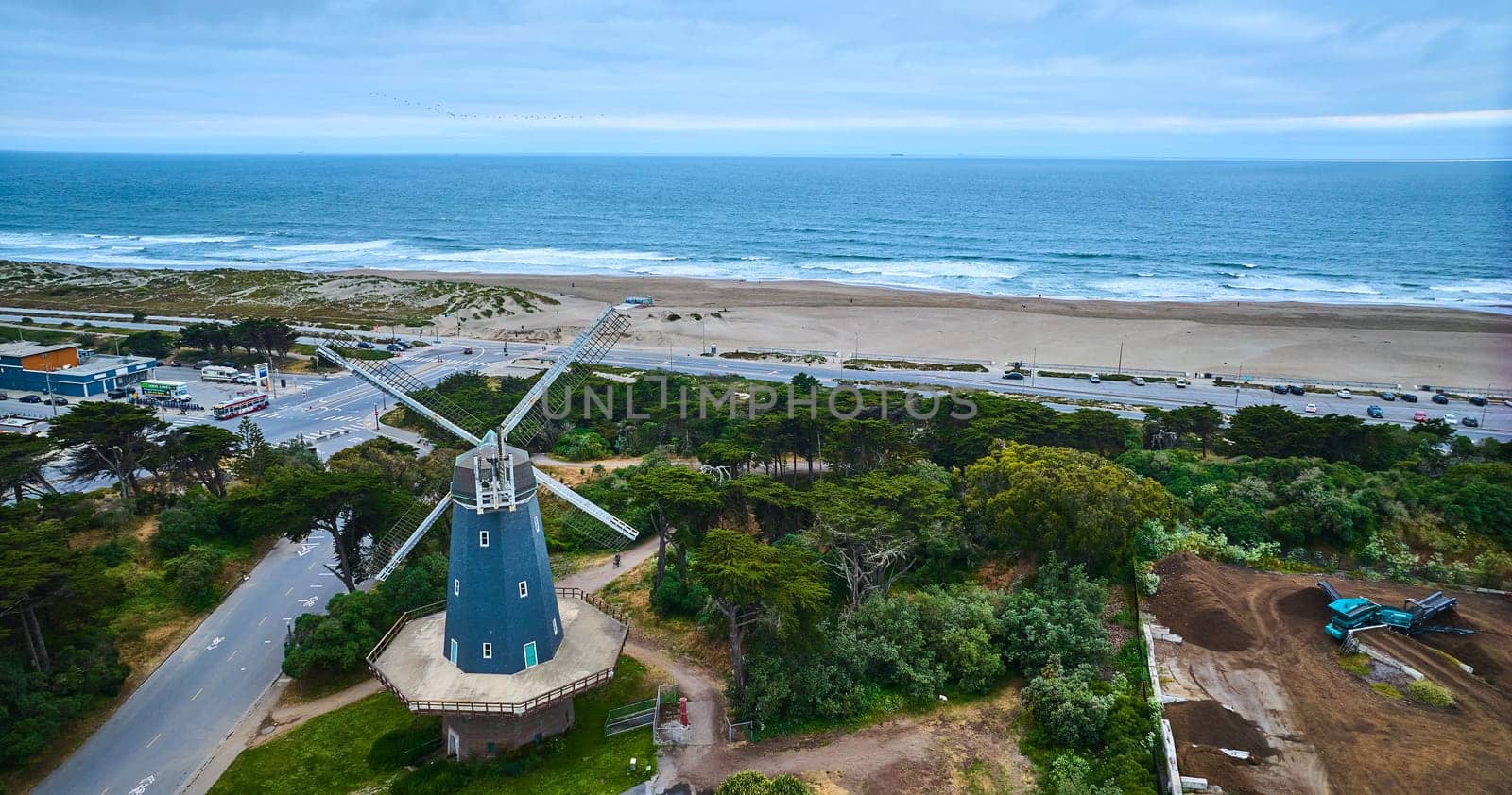Image of Aerial blue murphy windmill with white blades in grove of trees with sandy beach and ocean waves