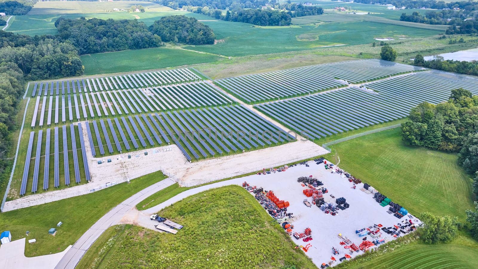 Image of Aerial of large solar farm with nearby lot full of construction equipment parts