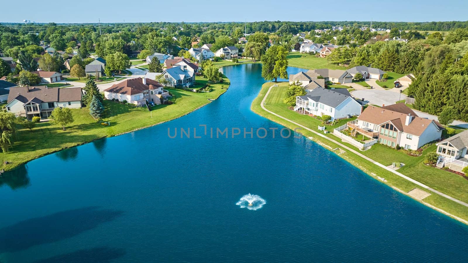 Image of Large pond with water fountain aerial over neighborhood with large expensive houses