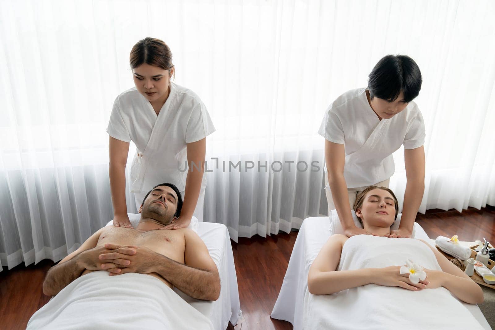 Caucasian couple customer enjoying relaxing anti-stress spa massage and pampering with beauty skin recreation leisure in day light ambient salon spa at luxury resort or hotel. Quiescent