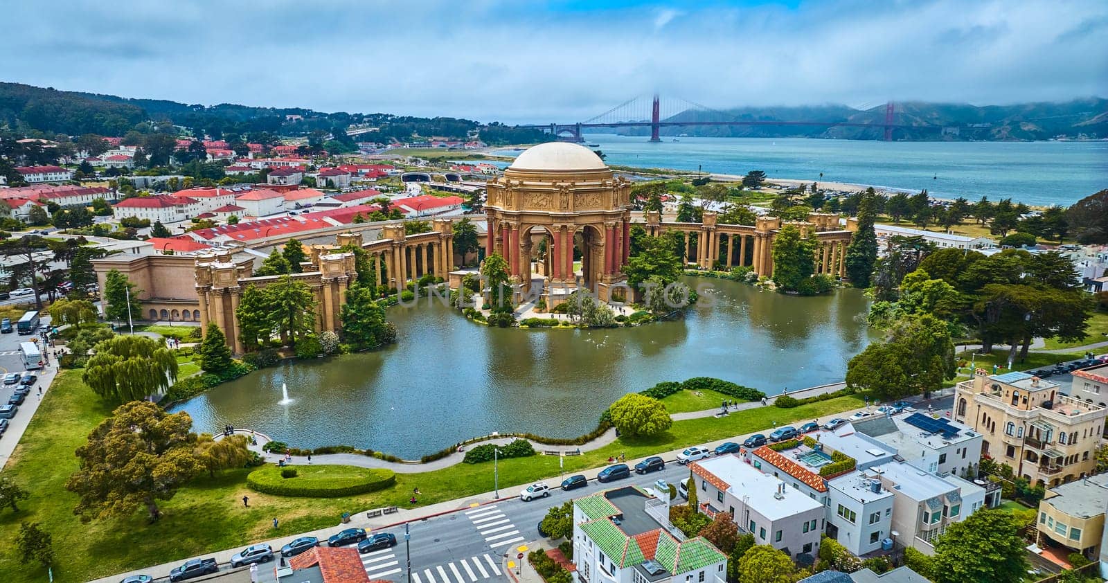 Image of Aerial Palace of Fine Arts colonnade and open rotunda on pond with city and Golden Gate Bridge