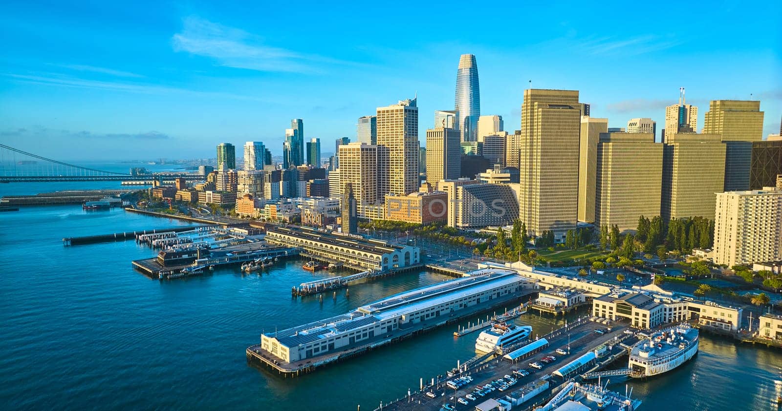 Image of Aerial golden lighting over water and boats at piers with San Francisco skyscraper skyline