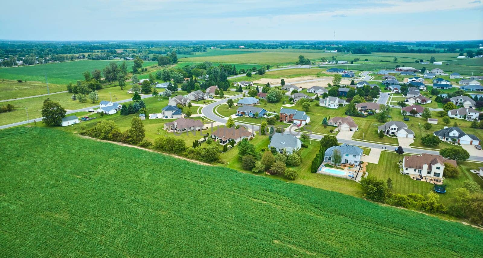 Image of Crops in farmland field giving way to rural neighborhood with suburban styled homes aerial