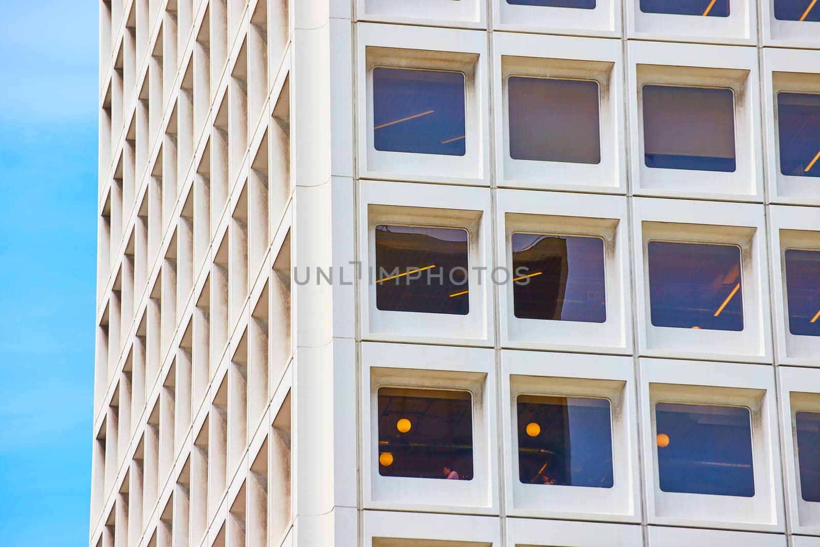 Image of Square windows on skyscraper zoomed in view on bright blue sky day with people in office