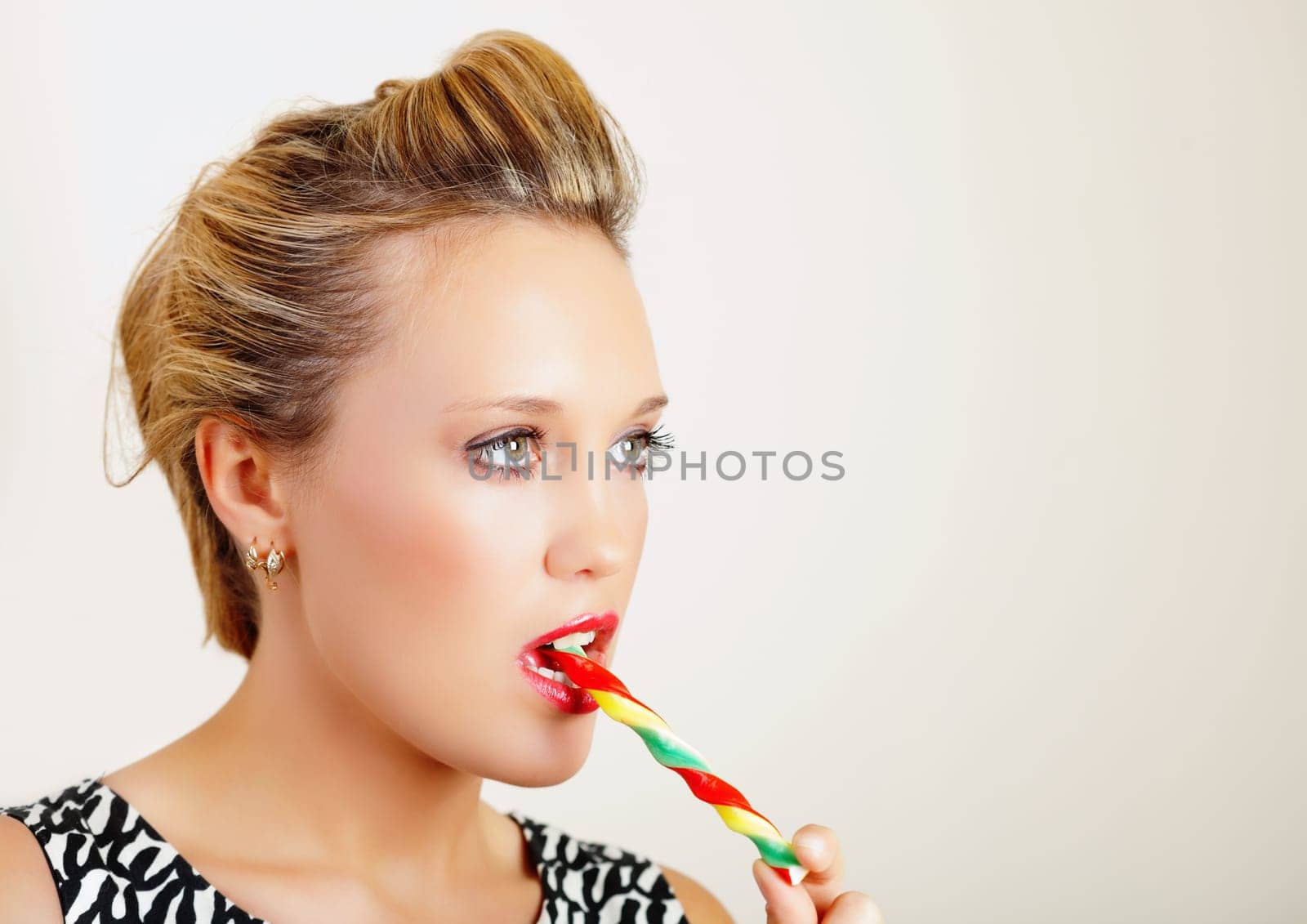 Portrait of a pretty young woman biting colorful lollipop