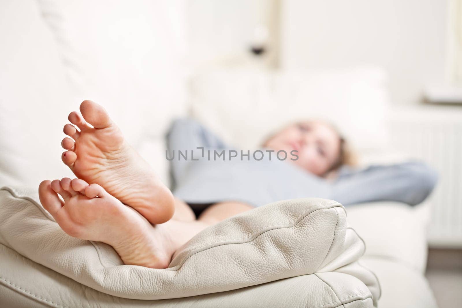 Barefoot young woman lying on sofa, shallow depth of field, focus on foot soles