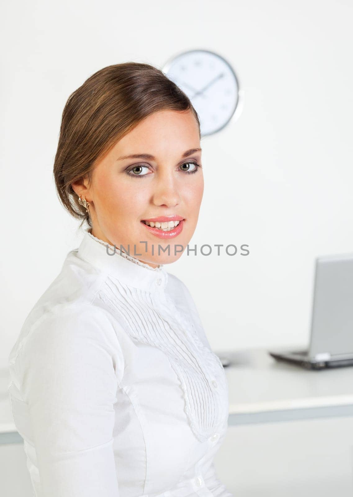 Young pretty smiling businesswoman standing in front of her desk in the office