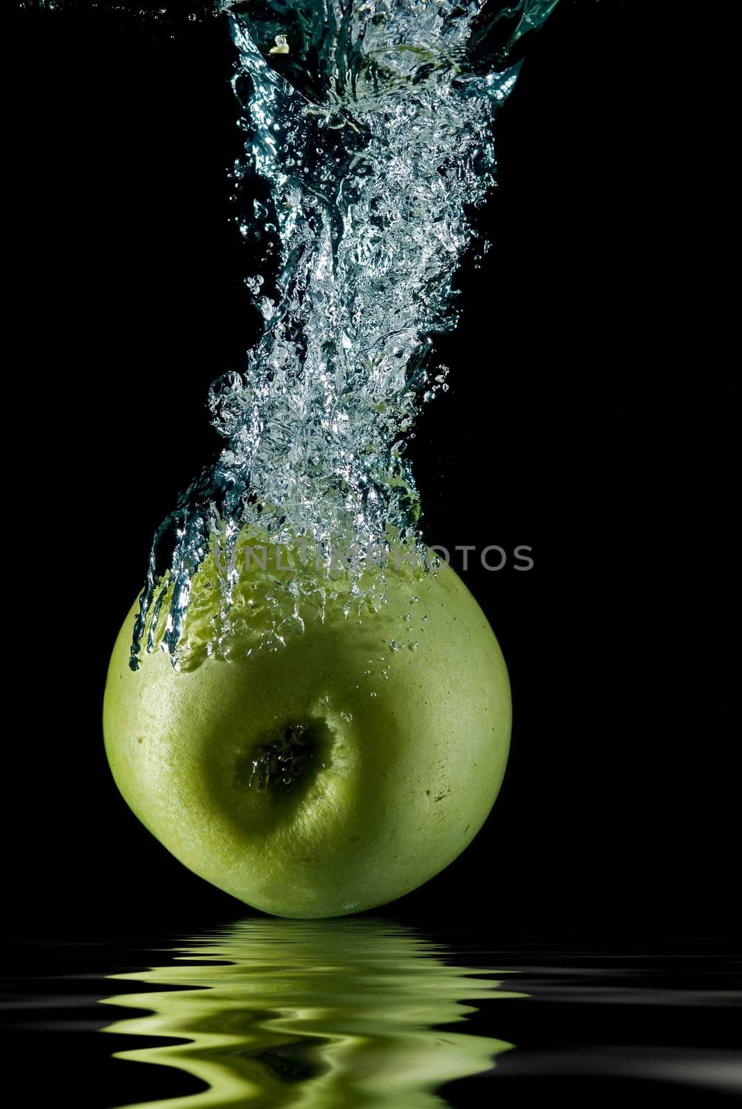 A green apple splashing on a water surface with a black background.