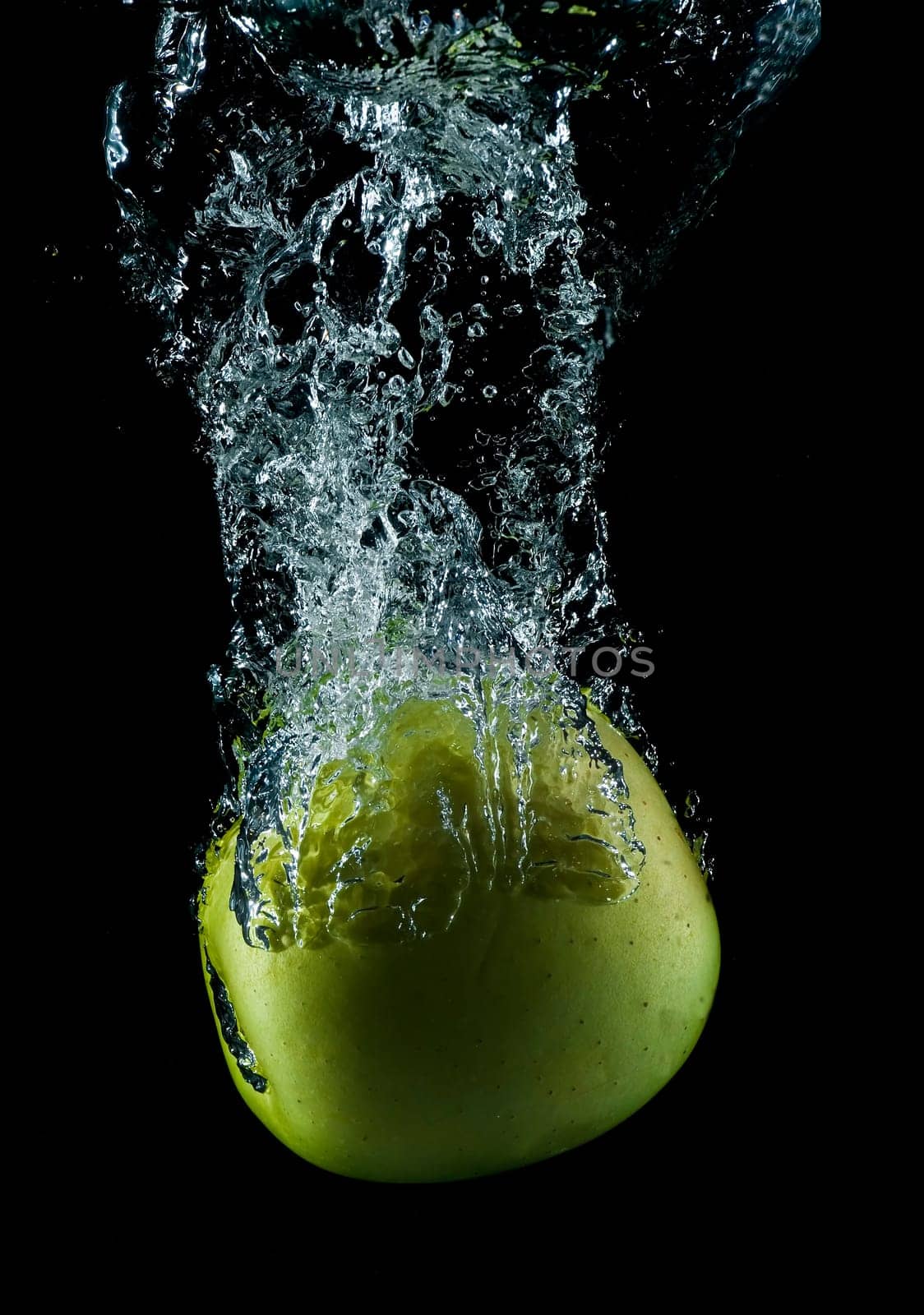 A green apple splashing on a water surface with a black background.