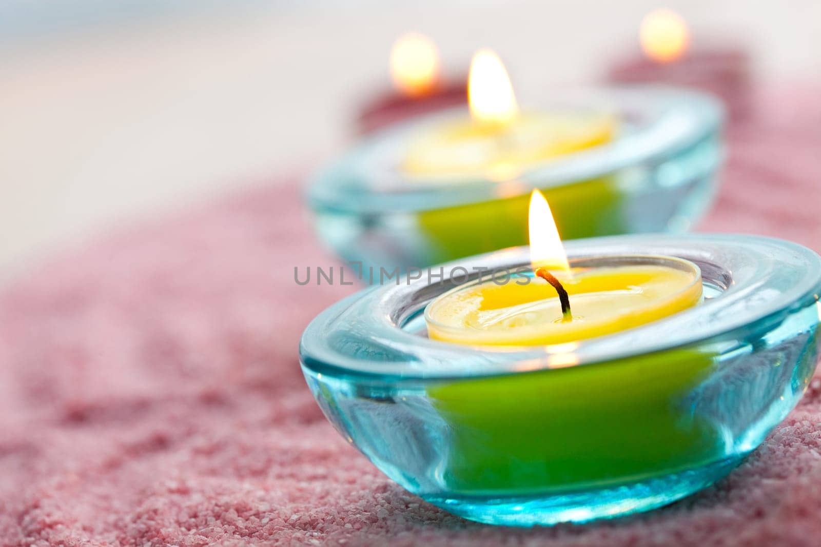 Close-up of yellow candles in glass holders on pink sand