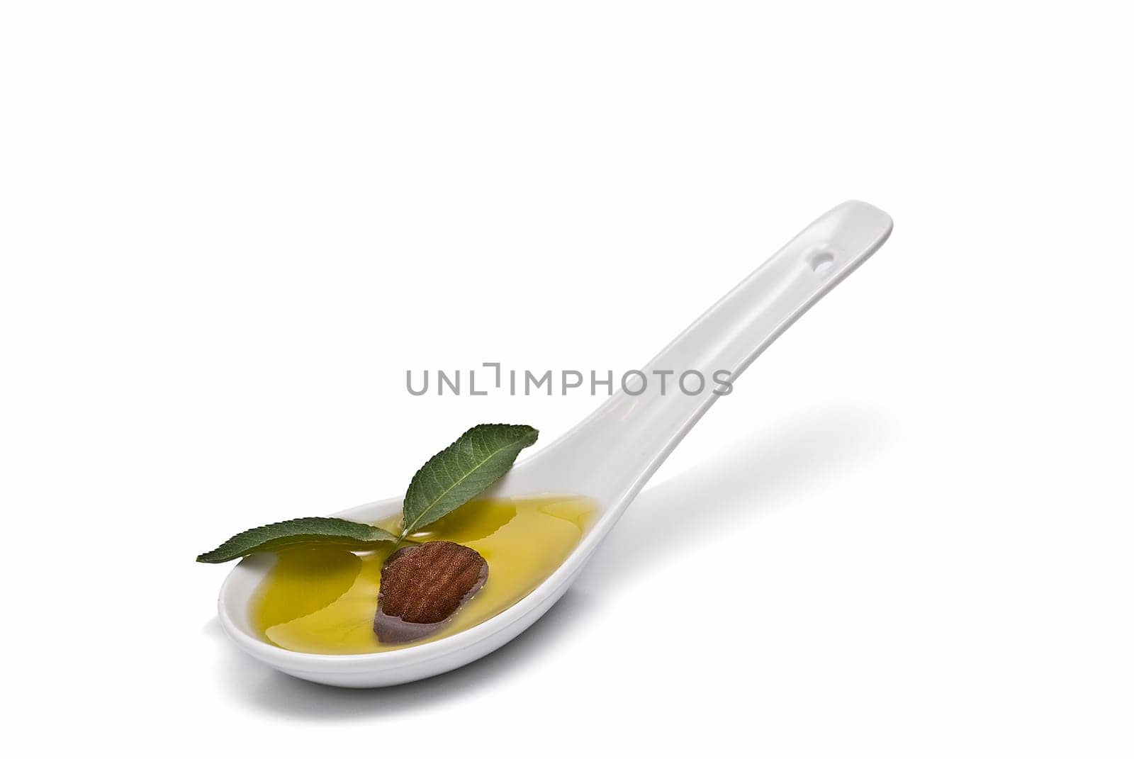 Almonds and a spoon with its oil over a white background.